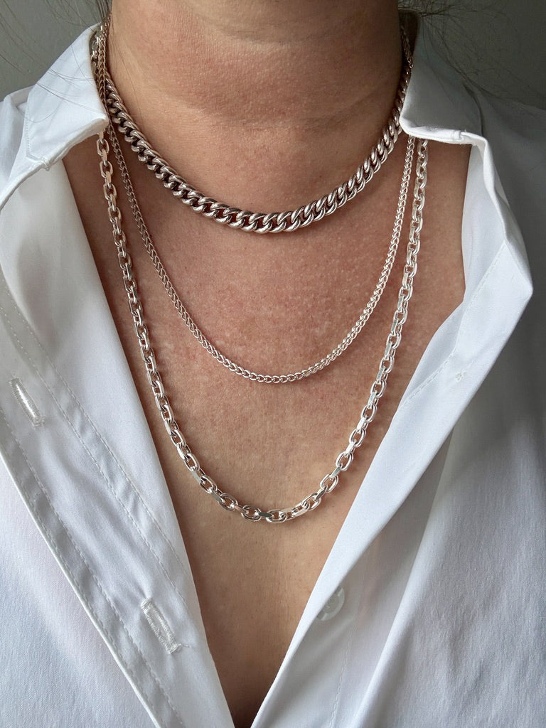 Close-up of a person wearing multiple silver chain necklaces with a white shirt.