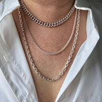 Close-up of a person wearing multiple silver chain necklaces with a white shirt.