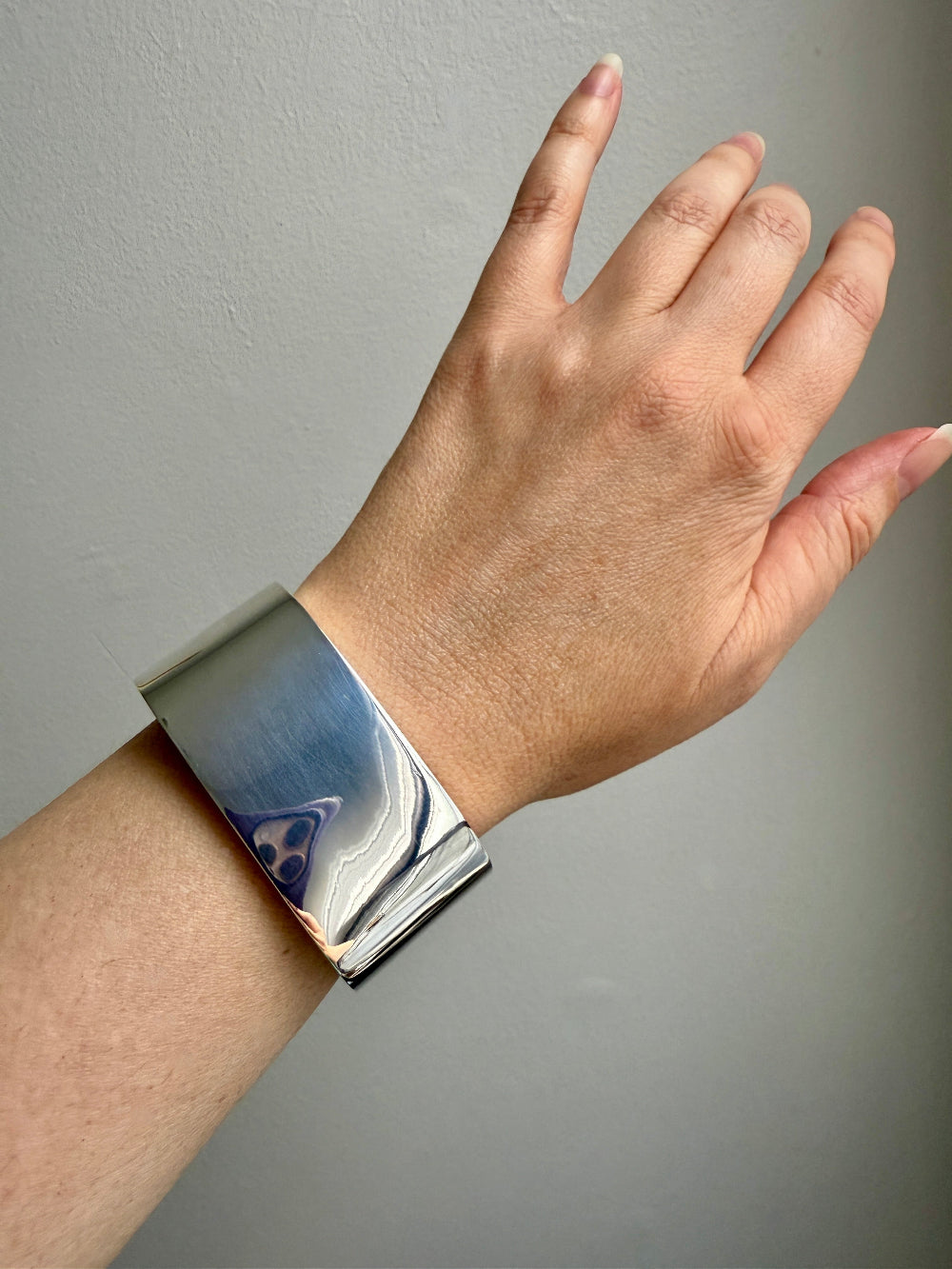 Silver bracelet on a wrist against a gray background