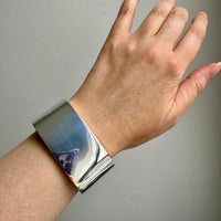 Silver bracelet on a wrist against a gray background