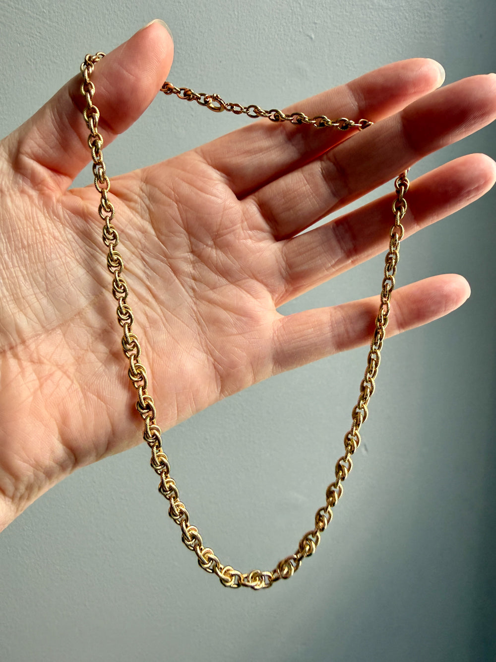 Gold chain held by a hand against a neutral background