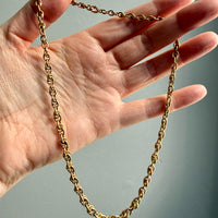 Gold chain held by a hand against a neutral background