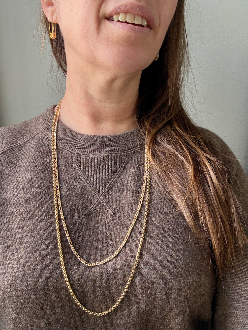Person wearing gold chain necklaces with a plain background