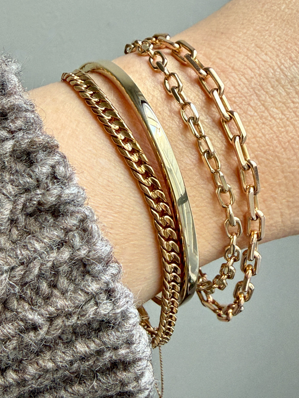 Gold chain bracelets on a wrist with a neutral background