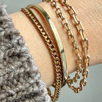Gold chain bracelets on a wrist with a neutral background