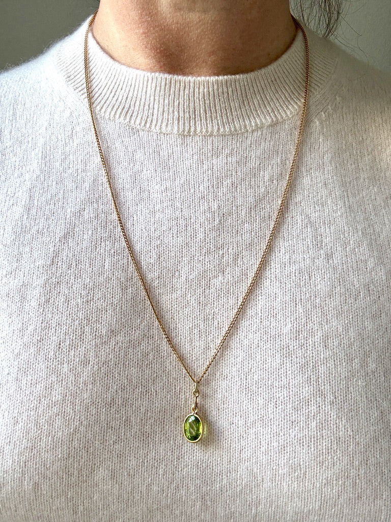 Necklace with a green pendant worn by a person in a light gray sweater.