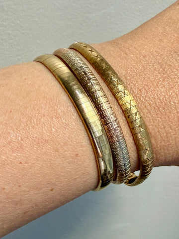 Close-up of a wrist wearing three gold bracelets on a neutral background