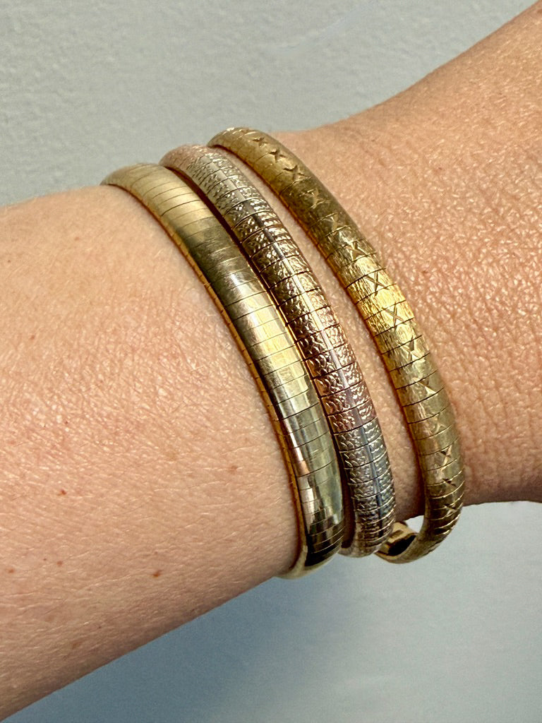 Close-up of a wrist wearing three gold bracelets on a neutral background