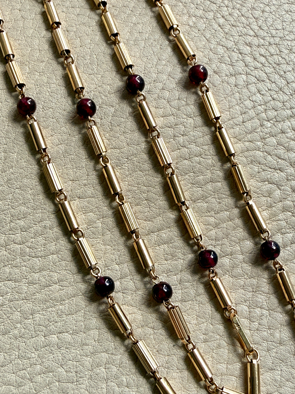 Gold chain necklace with dark red beads on a textured surface