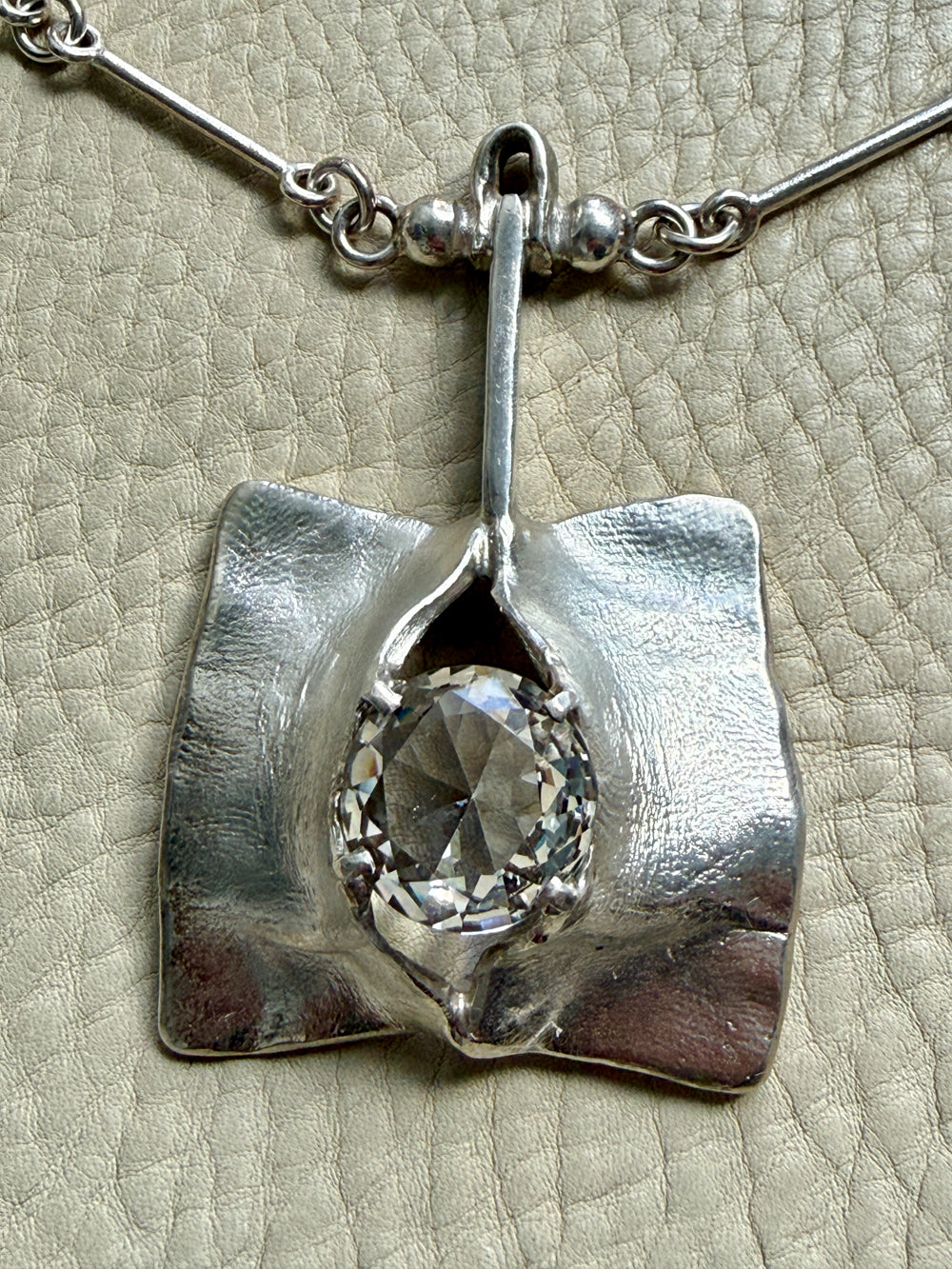 Silver pendant with a central gemstone on a textured beige background