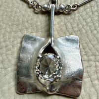 Silver pendant with a central gemstone on a textured beige background