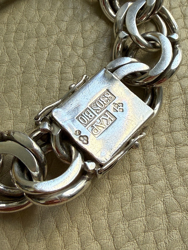 Close-up of a silver bracelet with a clasp on a beige textured background
