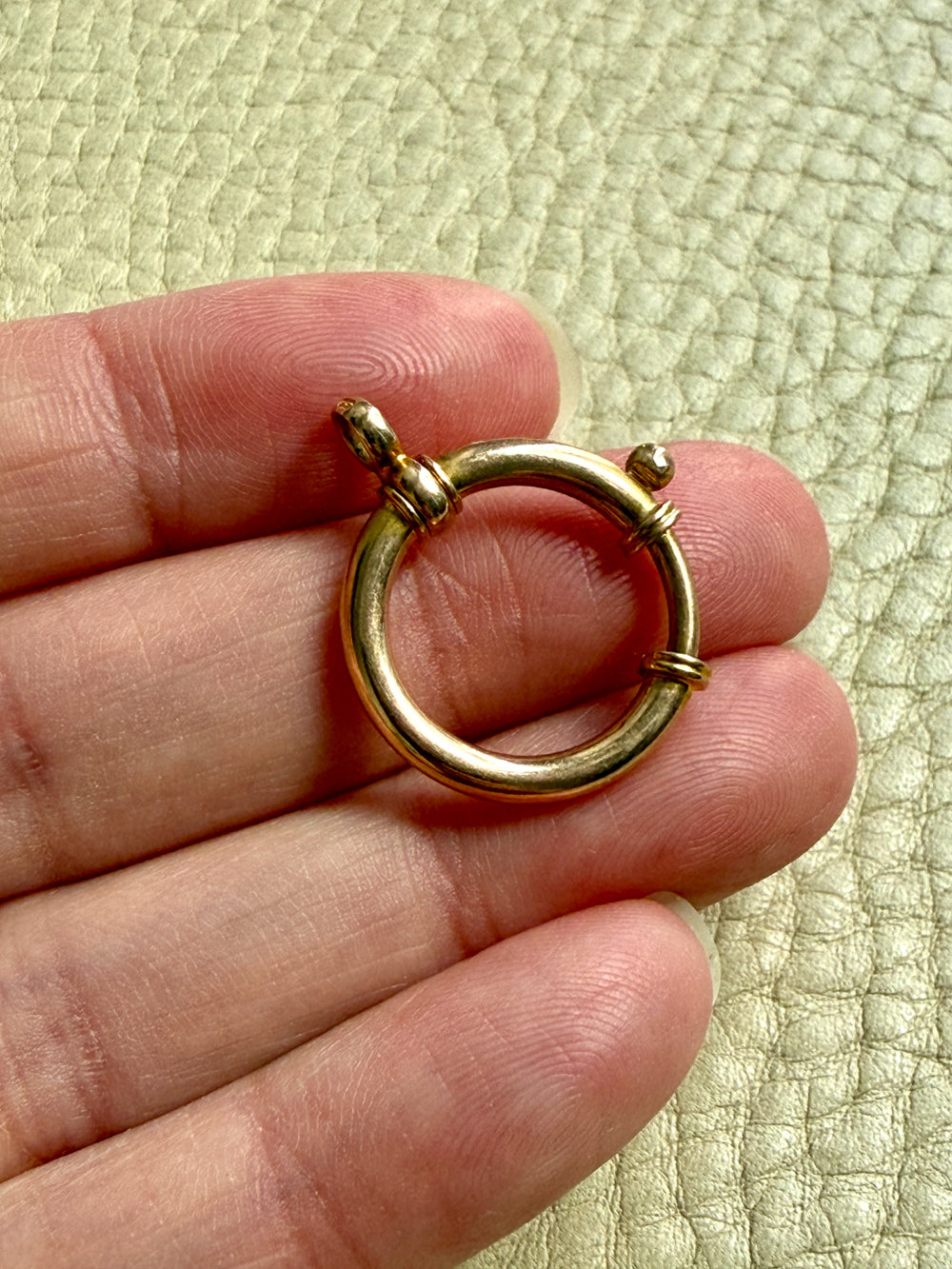 antique 18k gold large bolt clasp held between fingers against a textured light green background