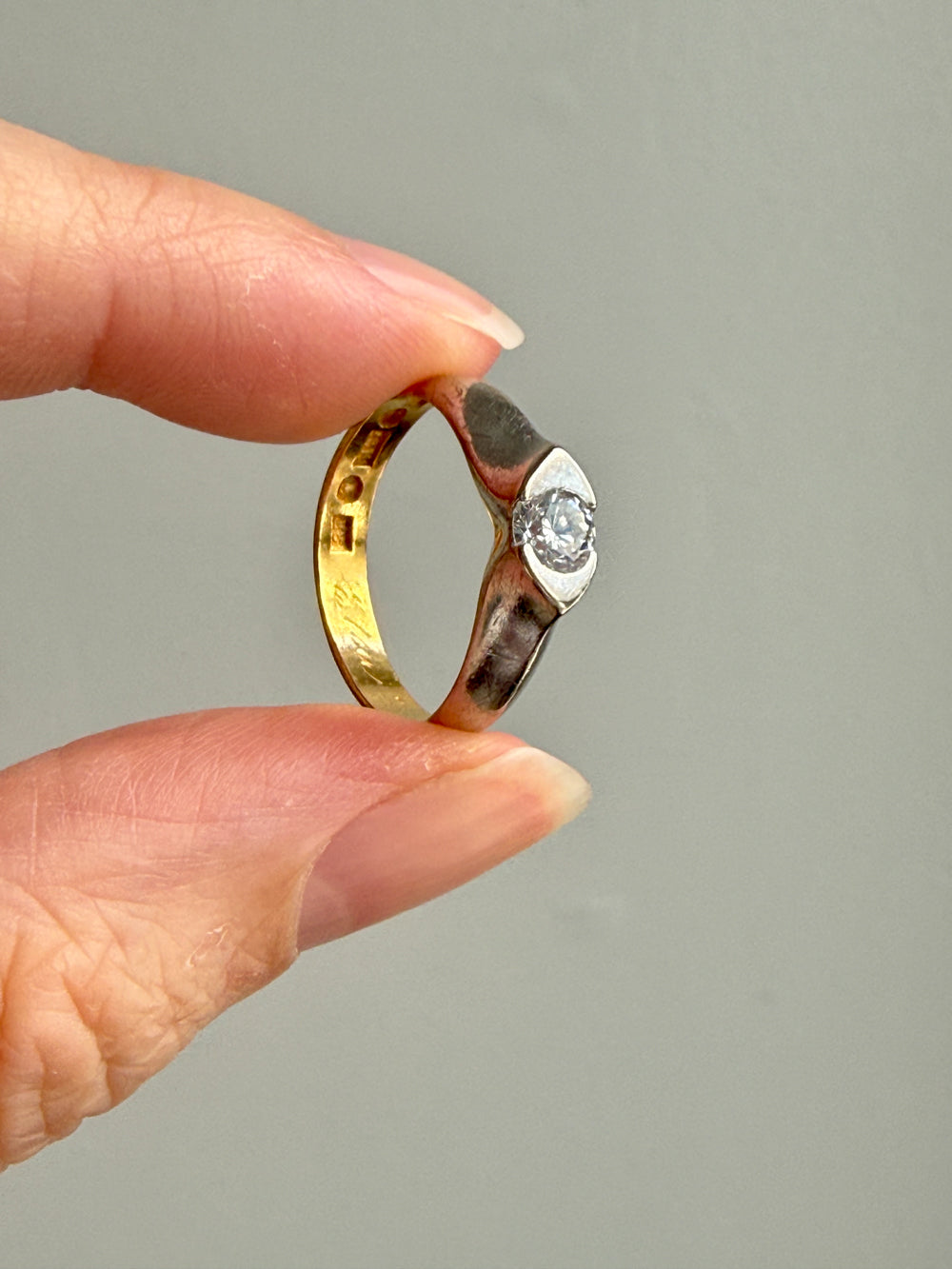 A close-up of a hand holding a two-tone ring with a yellow gold band, a silver-toned textured band, and a clear diamond