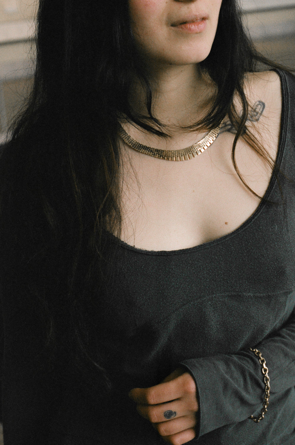 Person wearing a black top with vintage real gold necklace and bracelet and tattoos visible on neck and shoulder.