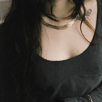 Person wearing a black top with vintage real gold necklace and bracelet and tattoos visible on neck and shoulder.