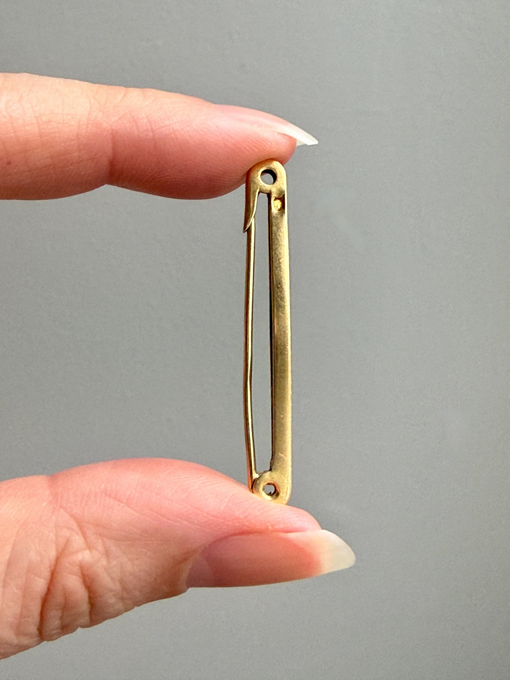 Gold safety pin held between fingers against a gray background