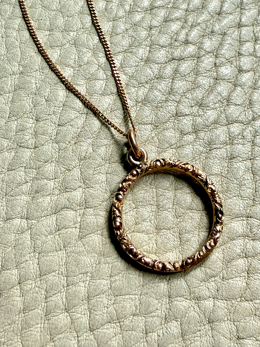 18k gold circular pendant necklace on a textured light green surface