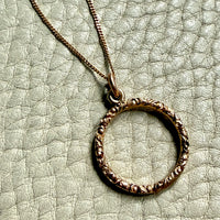 18k gold circular pendant necklace on a textured light green surface