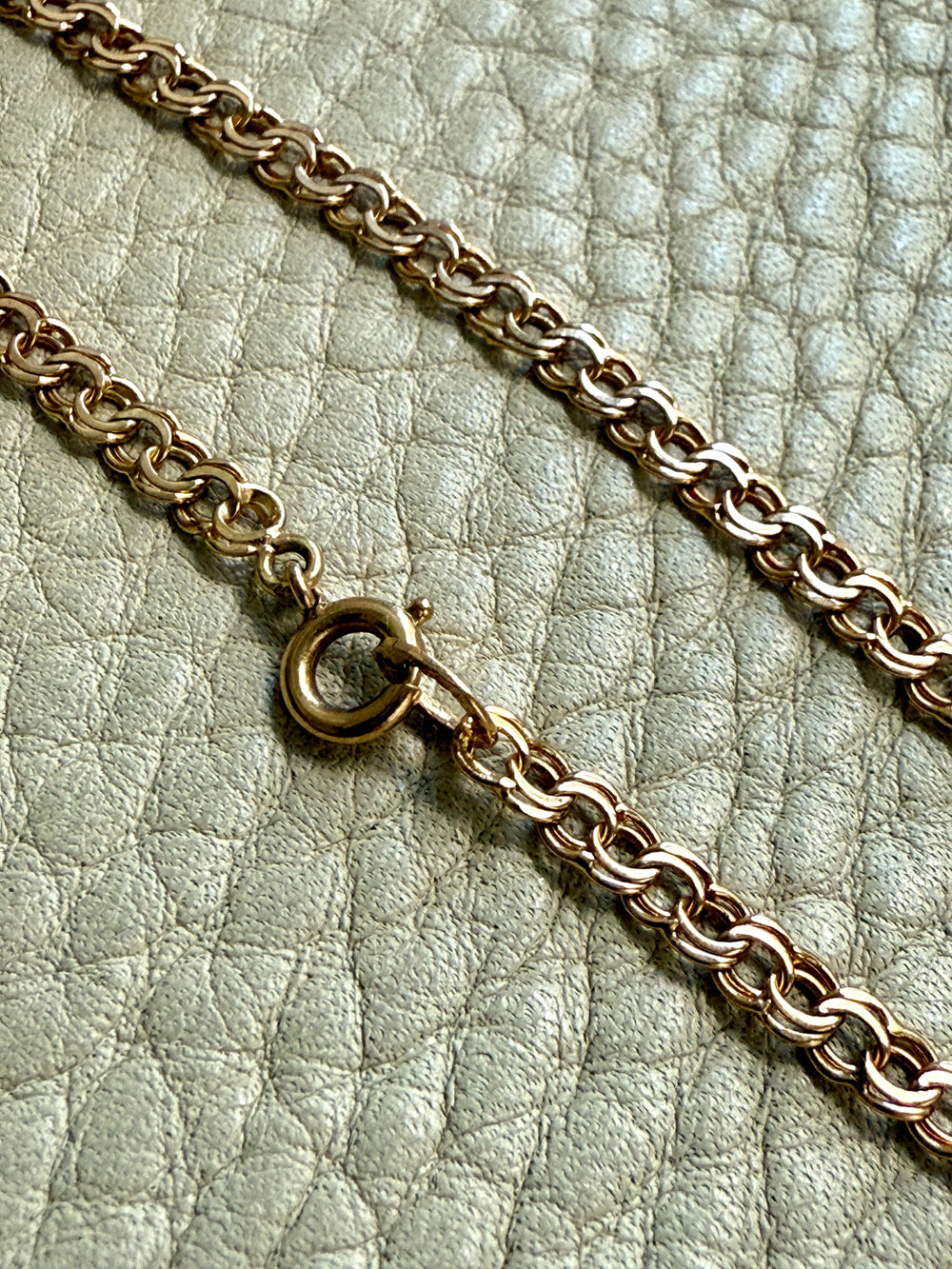 Gold chain bracelet on a textured light green surface