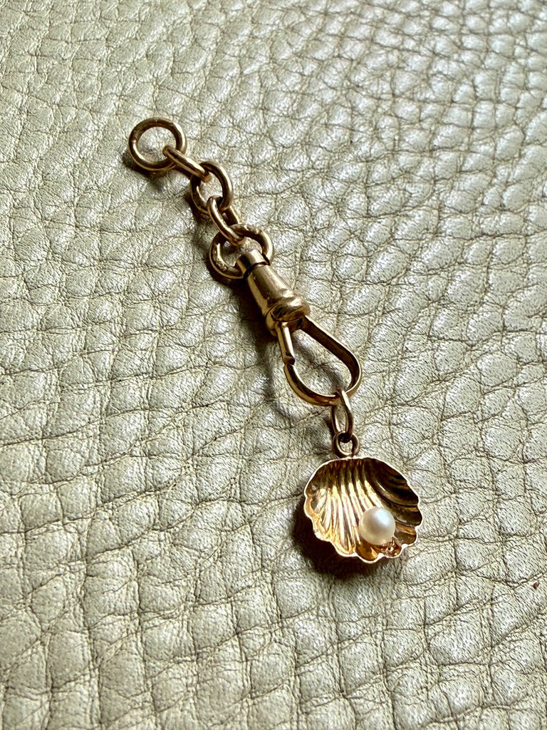Gold charm with a shell and pearl on a textured beige background