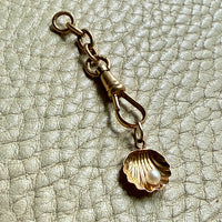 Gold charm with a shell and pearl on a textured beige background