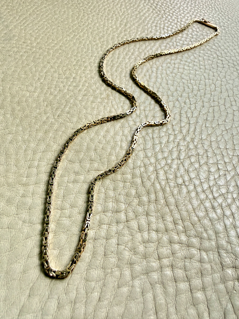 14k gold Gold byzantine chain necklace on a textured beige surface penelopepenelope.com fine jewelry