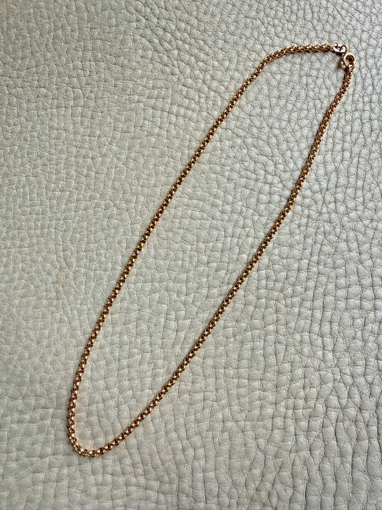Gold chain necklace on a textured light gray surface