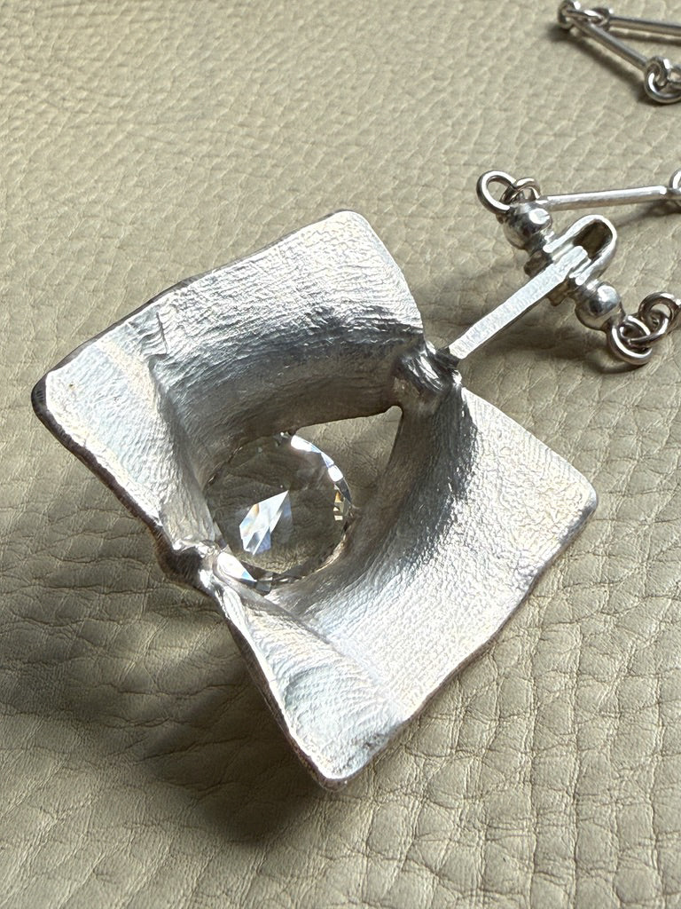 Silver pendant with a clear gemstone on a textured beige surface