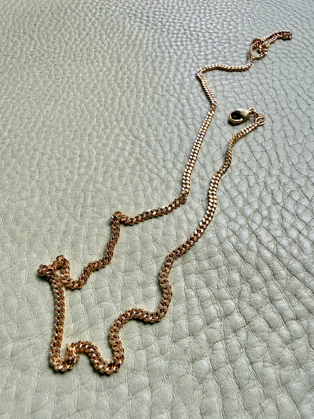 18k Gold curb chain necklace on a textured light blue surface