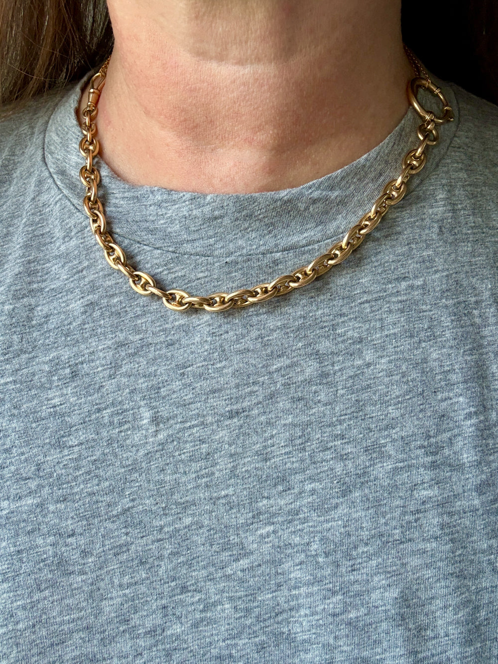 Gold chain necklace on a person wearing a gray shirt