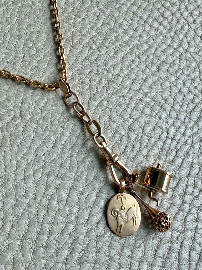 Gold necklace with various charms on a textured light gray background