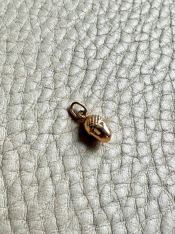 18k Gold acorn charm on a textured gray surface
