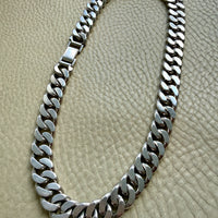 A vintage silver weighty curb link chain necklace displayed on a textured beige leather surface.