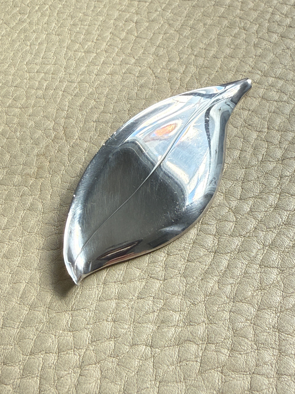 Silver leaf-shaped vintage brooch on a textured beige surface