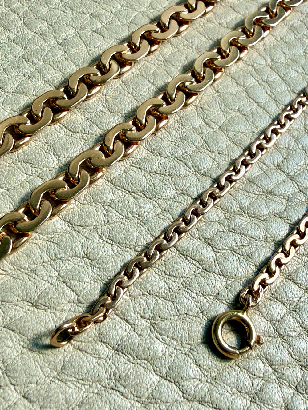 Two gold chains on a light green textured surface