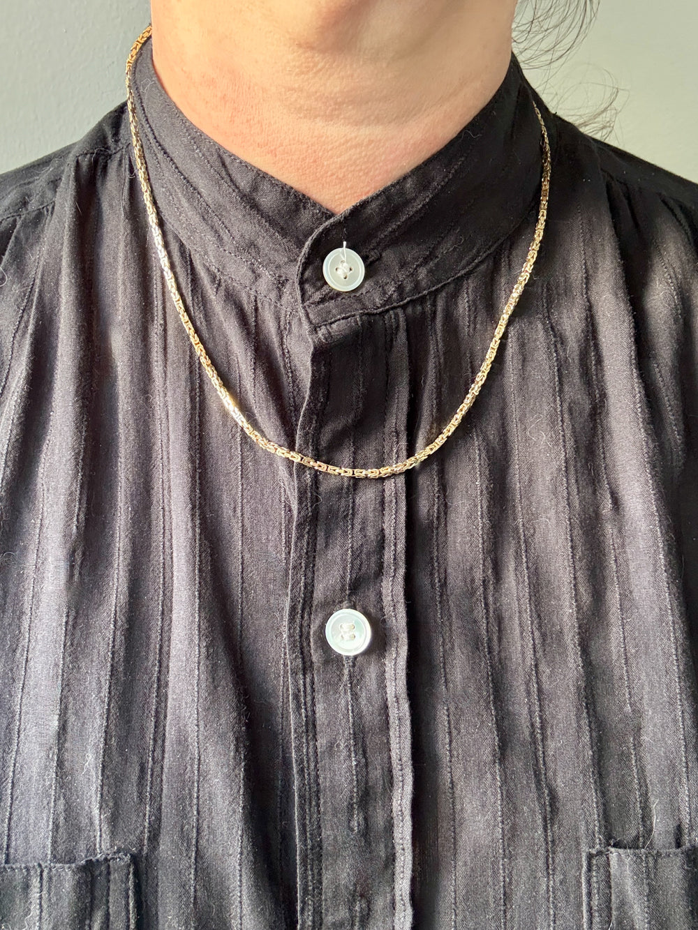 Person wearing a dark shirt with a gold chain necklace 