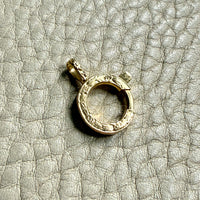 Gold bolt clasp pendant on a textured gray surface