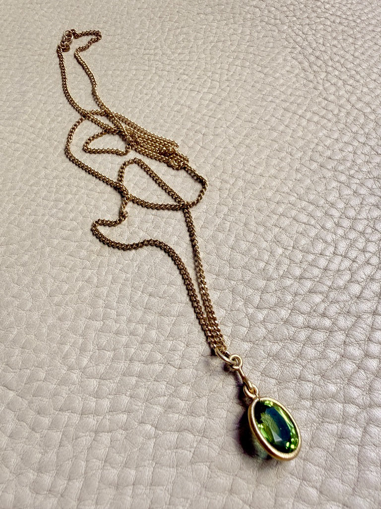 Gold necklace with a green pendant on a textured beige surface