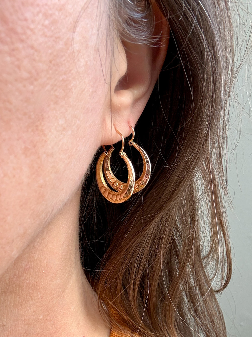 Close-up of a person wearing gold hoop earrings with a neutral background