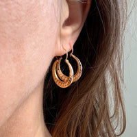 Close-up of a person wearing gold hoop earrings with a neutral background
