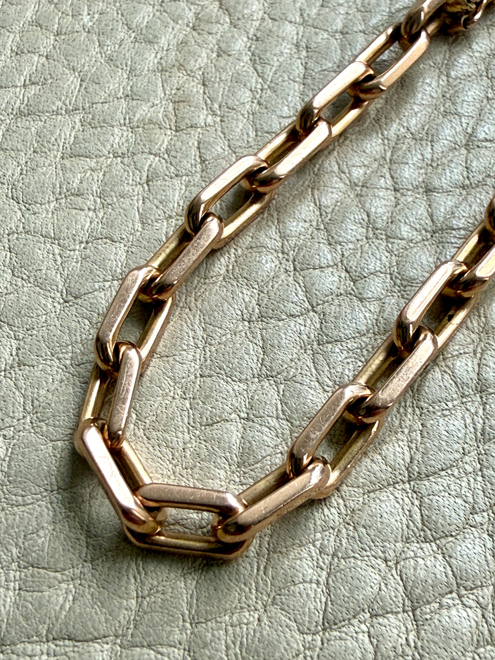 Gold chain bracelet on a textured light green surface
