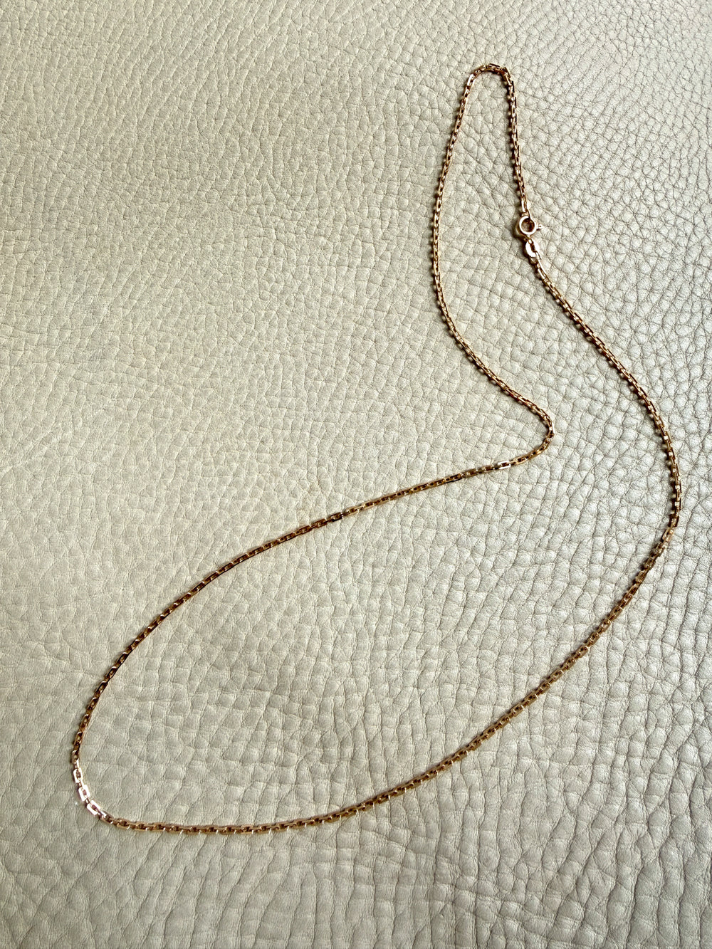 Gold chain necklace on a textured beige surface