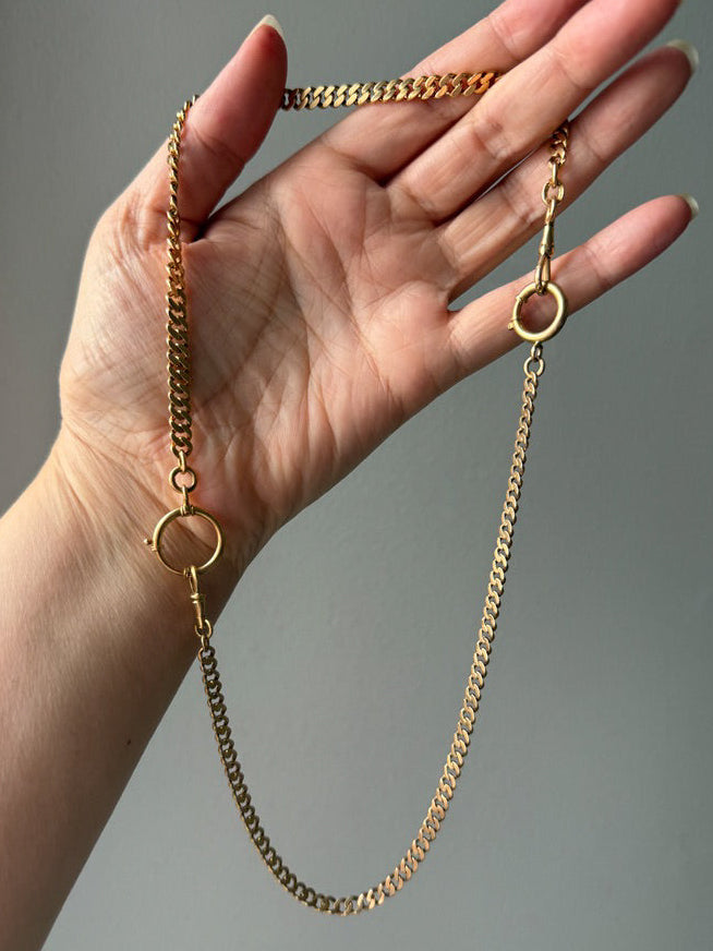 Gold watch chain necklace held in a hand against a gray background. PenelopePenelope.com