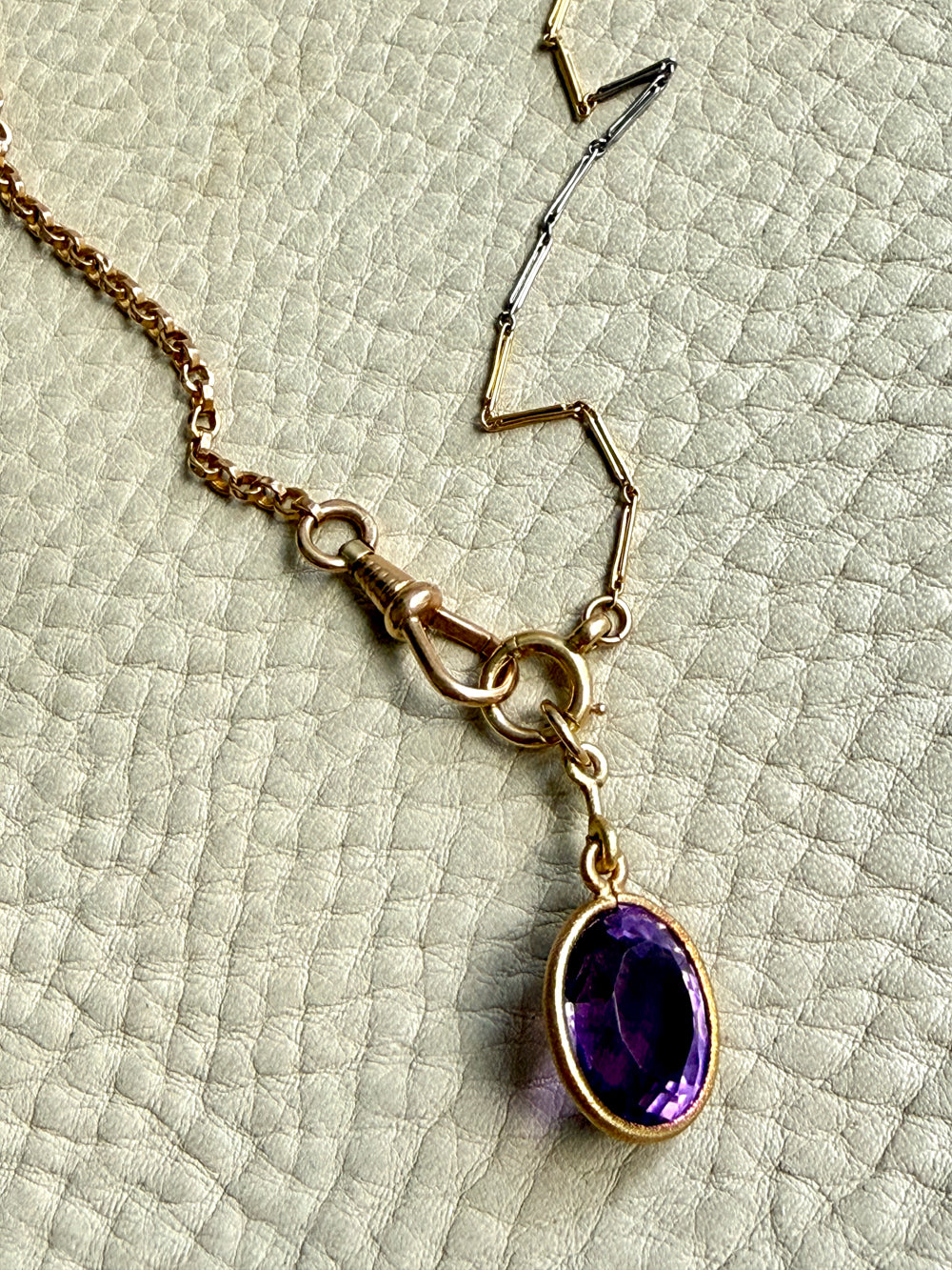 Gold necklace with a purple gemstone pendant on a textured green surface