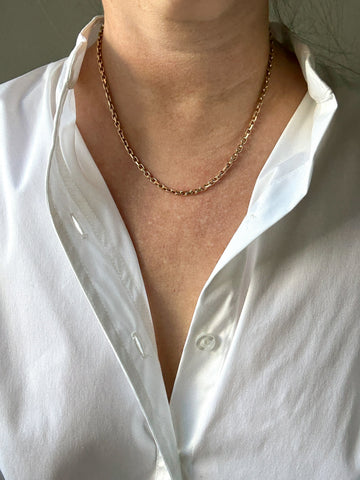 Person wearing a gold chain necklace with a white shirt