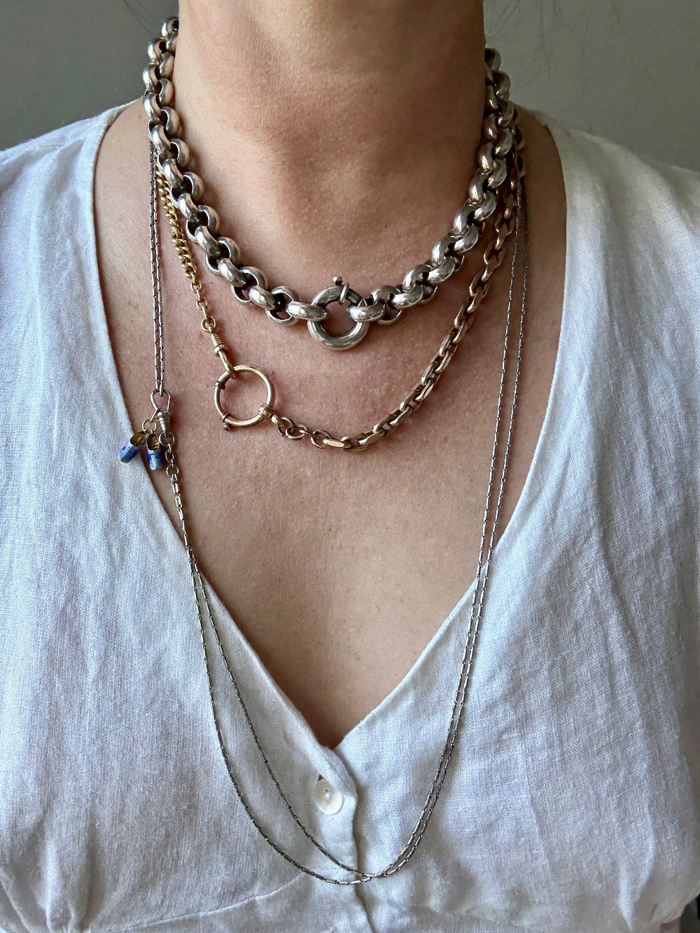 Person wearing multiple gold, silver and platinum necklaces on a plain background