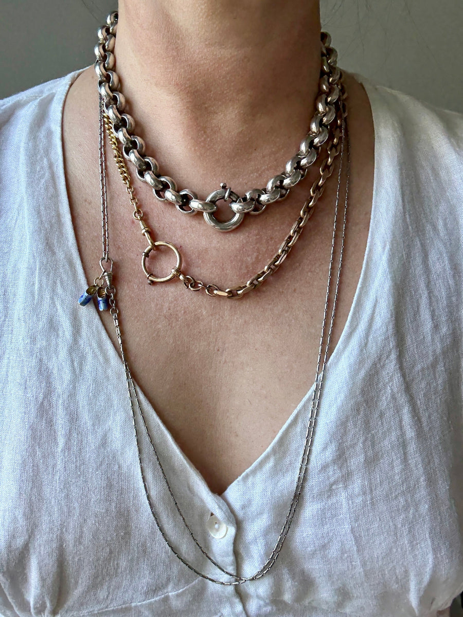 Person wearing multiple gold, silver and platinum necklaces on a plain background