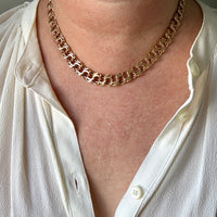 A close-up of a person wearing a chunky 18k gold chain necklace over a white button-up shirt.