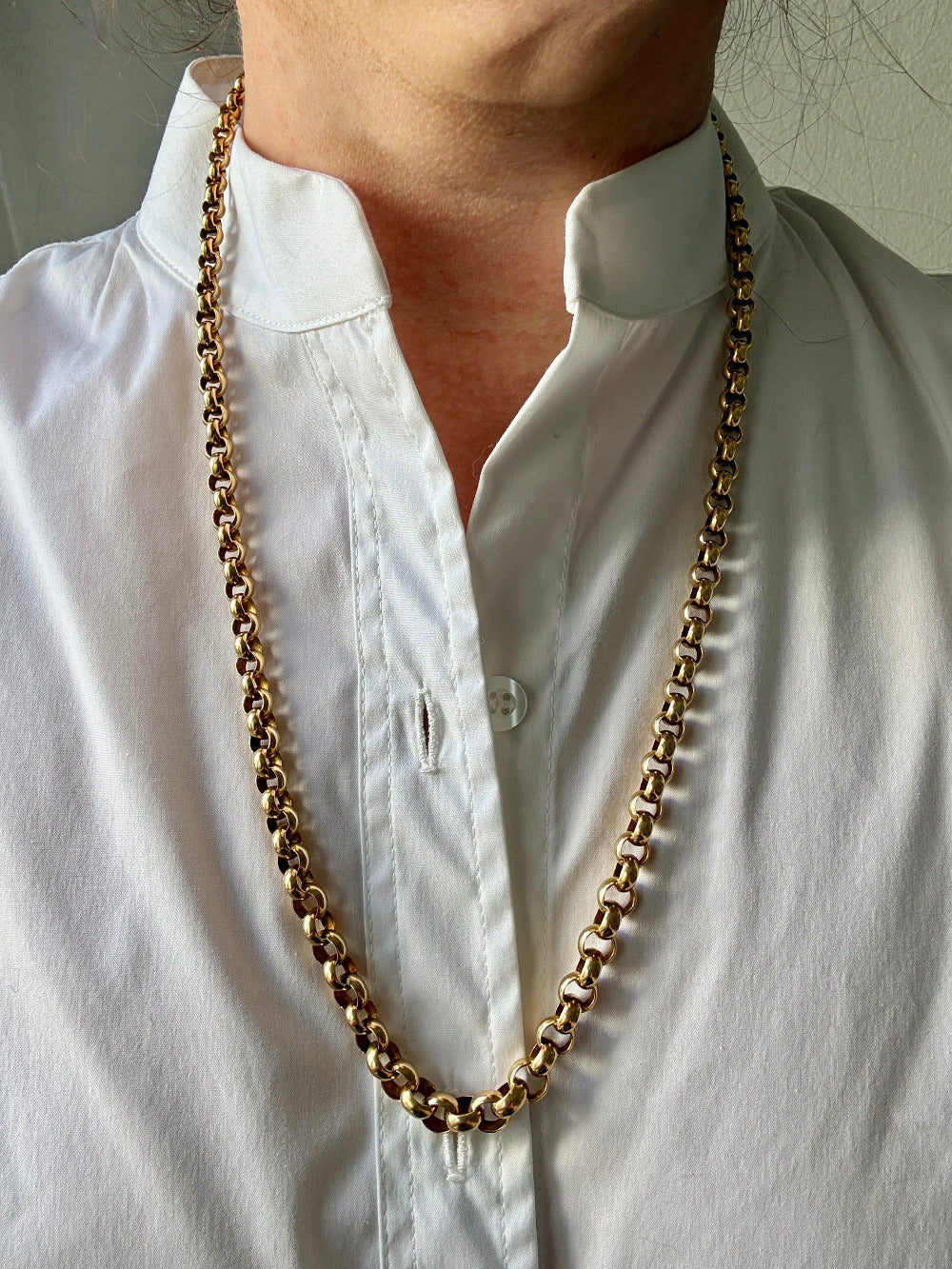 Person wearing a long gold chain necklace with a white shirt.